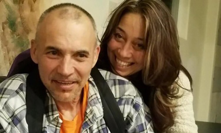 Joaquin and Diana A man with a buzz cut wearing a backpack smiles while a woman with long brown hair hugs him from behind and smiles widely