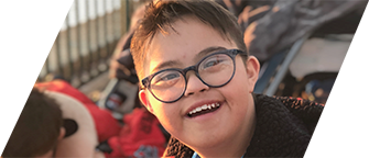 Close up of a Latino boy with Down syndrome wearing round glasses and an open-mouthed smile