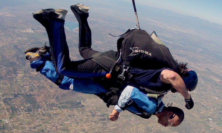 Tim skydiving An Asian man with a disability skydiving, strapped to an instructor
